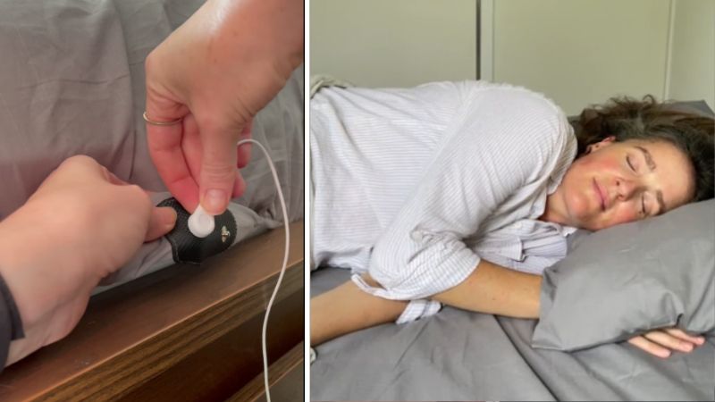 Person connecting a device to a bed and another sleeping on gray sheets.